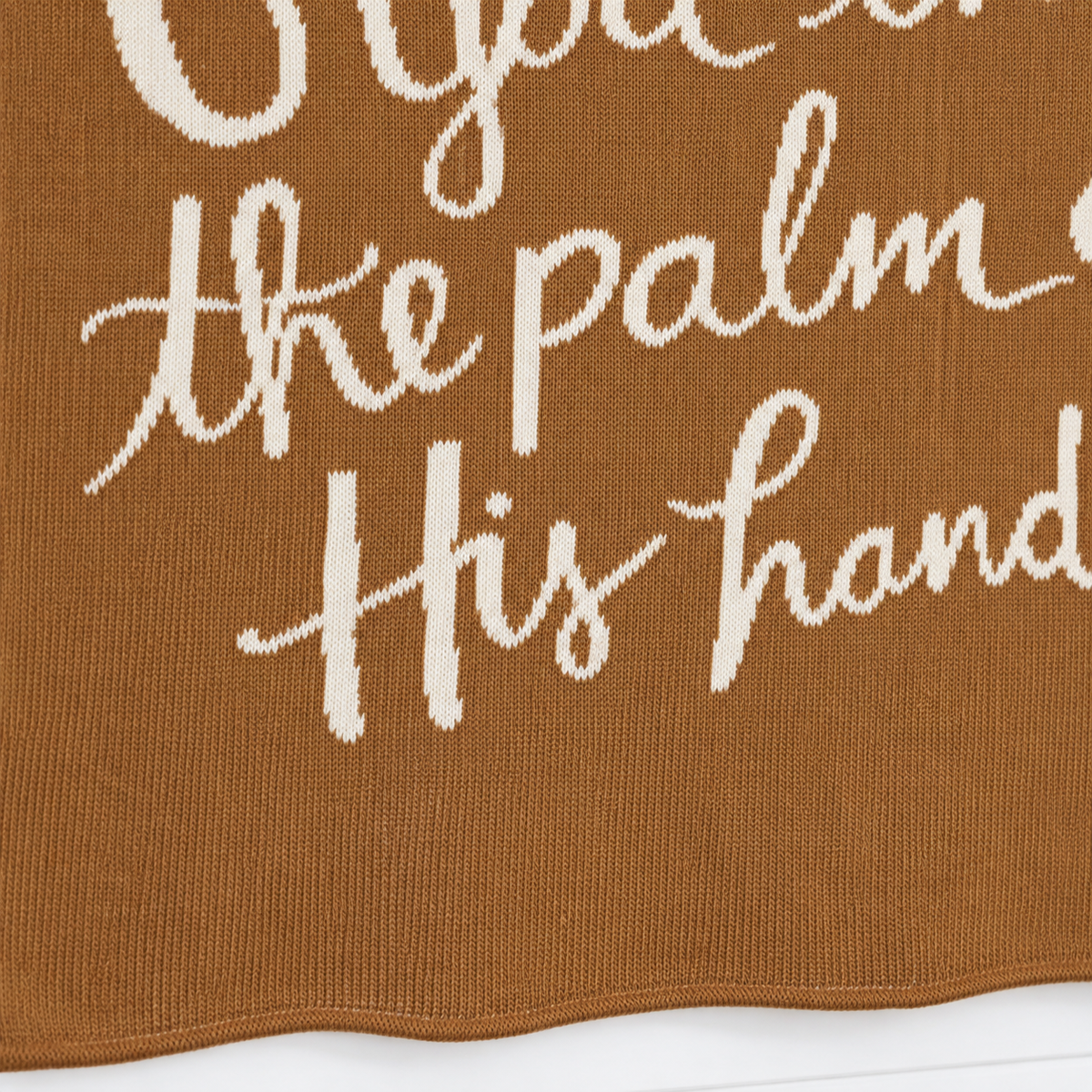 Caramel God Has You blanket close-up showing light knit lettering, fine stitches and the lower finished edge.