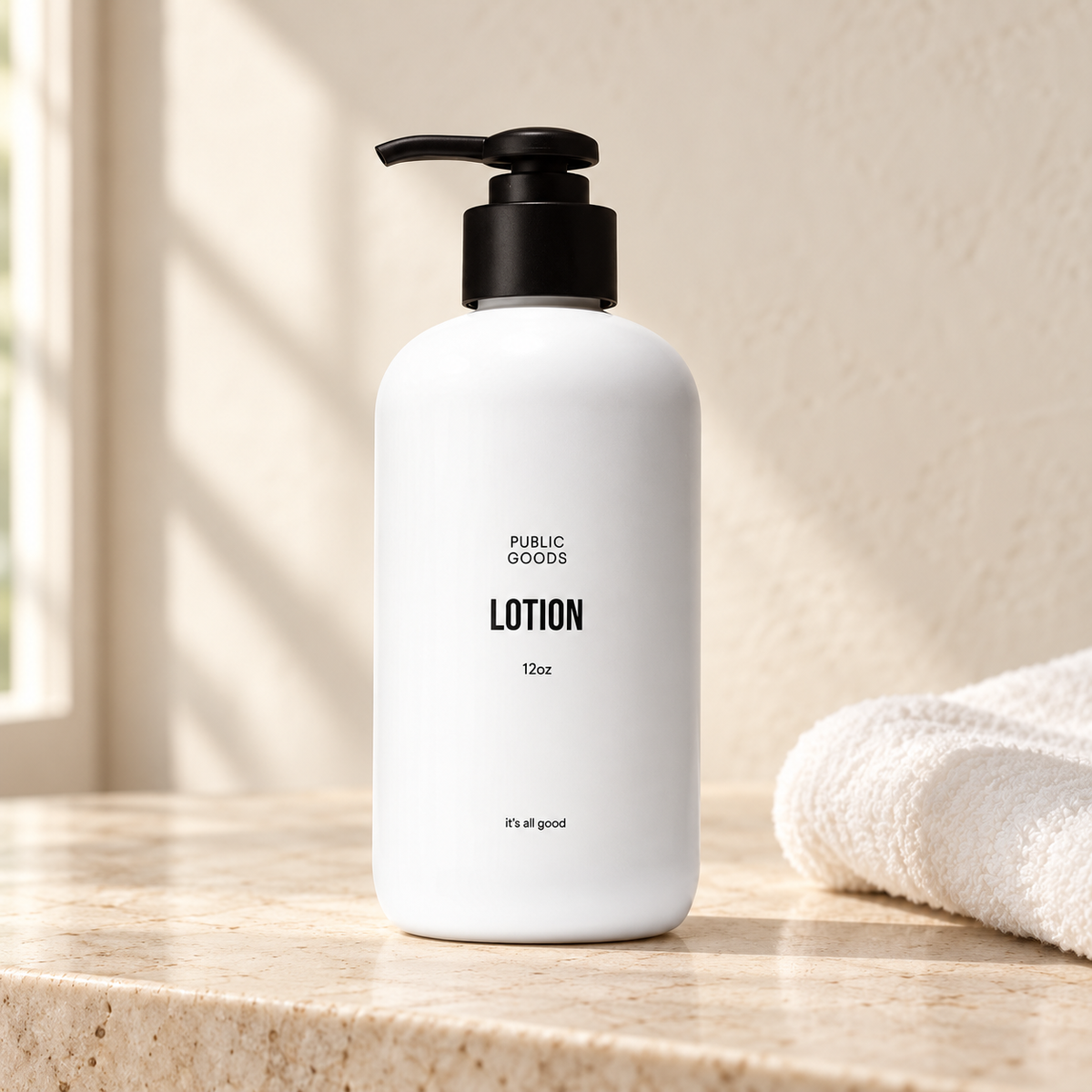 Public Goods 12 oz lotion bottle with black pump on a stone vanity beside a white towel.