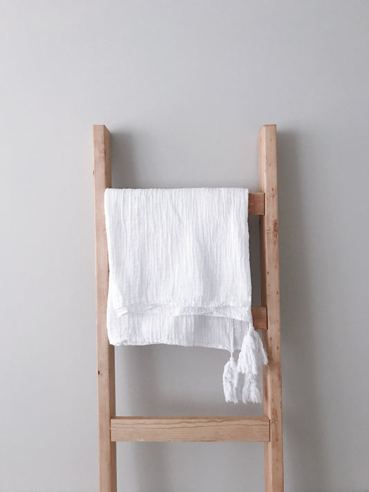 White tassel muslin throw folded over a wooden ladder