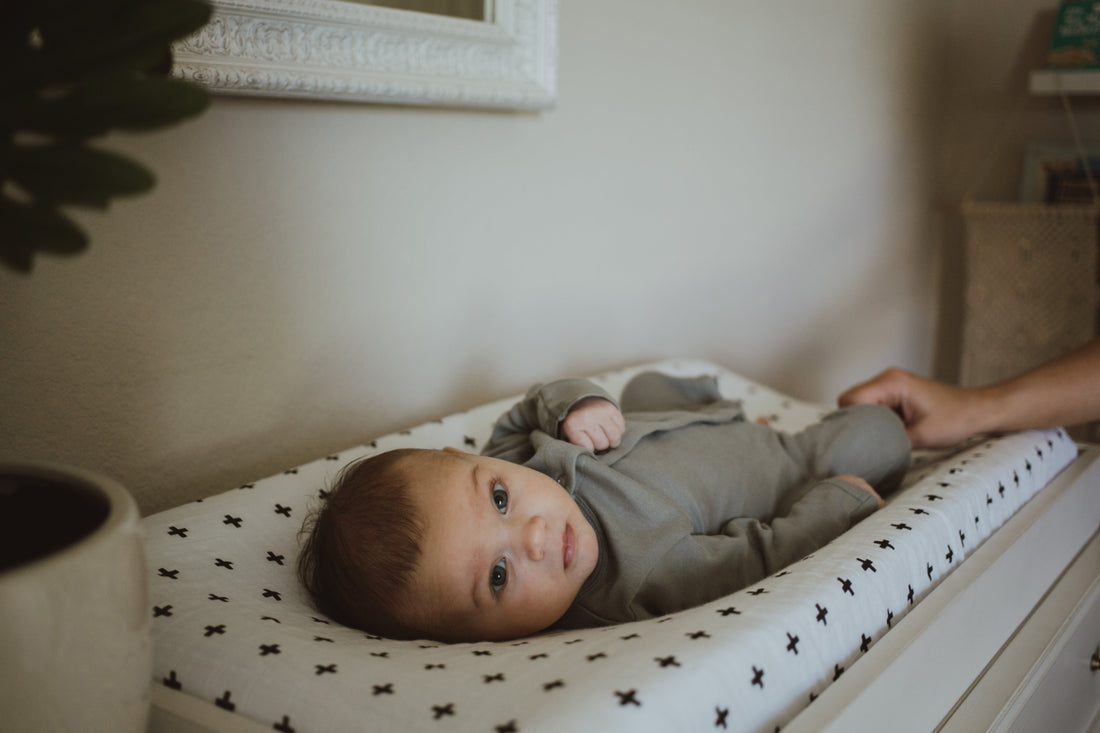 Baby in a gray coverall looking toward the camera during a change