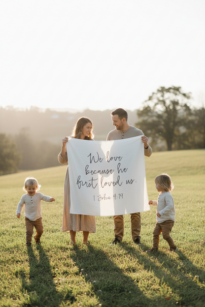Family holding up 1 John 4:19 Scripture Swaddle.