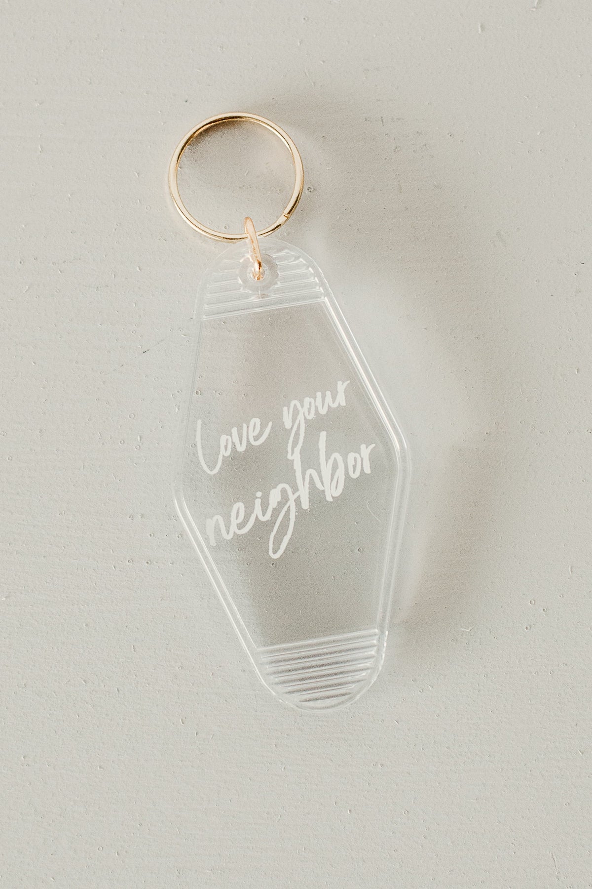 Love Your Neighbor clear keychain with white script and gold ring, original angled product photograph.