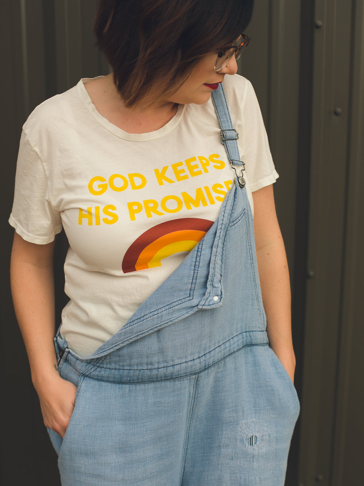 Woman wearing the God Keeps His Promises tee under denim overalls.