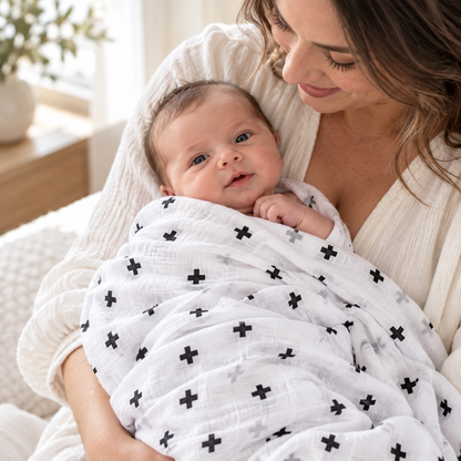 Mother holding a newborn in the white Swiss Cross muslin swaddle with black crosses.