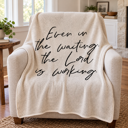 Even in the Waiting the Lord Is Working Natural knit blanket — styled on a linen reading chair.