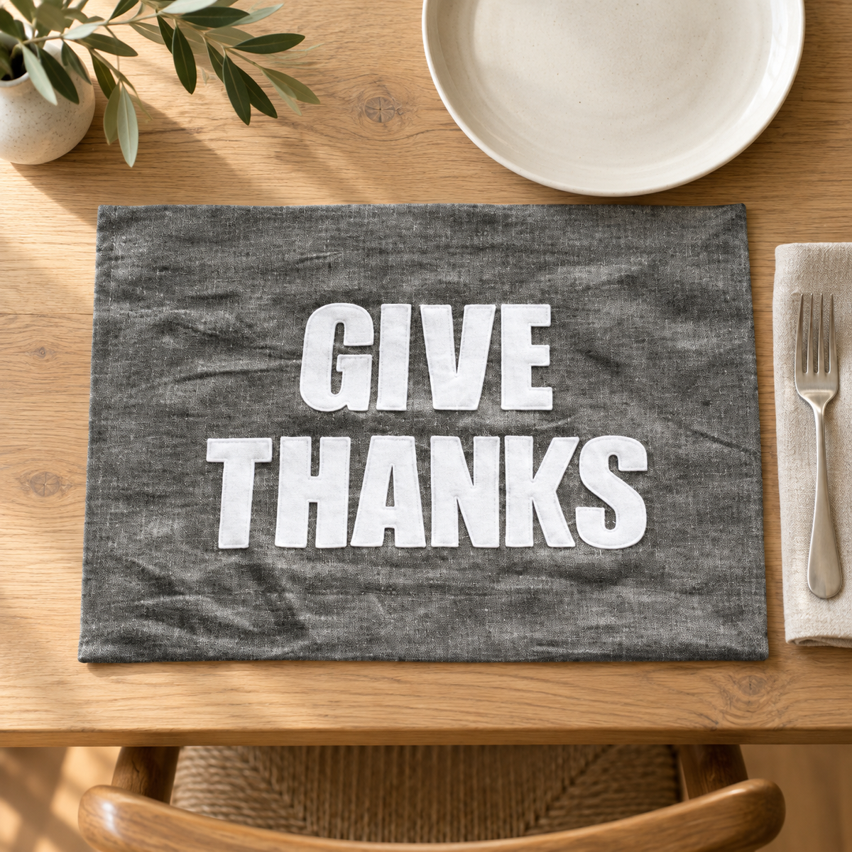 Graphite linen Give Thanks placemat with white lettering on a wood dining table.