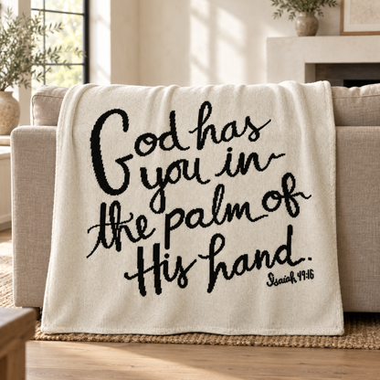 God Has You blanket in Natural with black hand-lettered artwork, draped over a linen sofa in a sunlit living room.