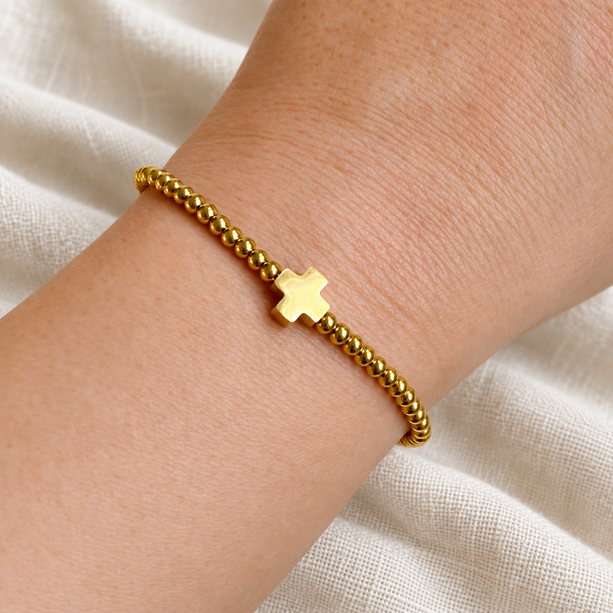Gold So Very Blessed cross bracelet worn on wrist against ivory linen