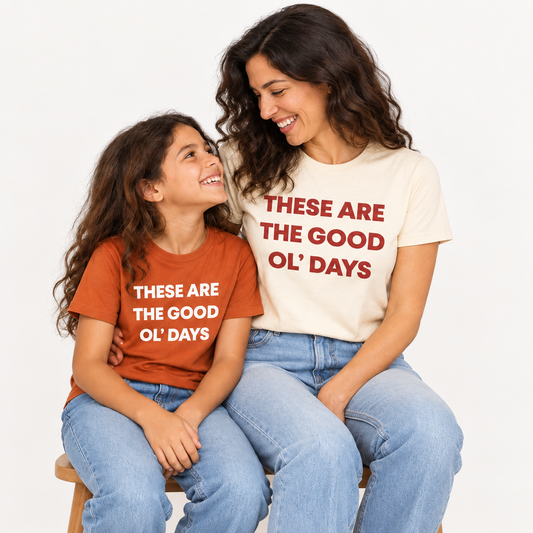 These Are the Good Ol’ Days Organic Unisex Tee | Cream worn by a mother alongside her child in the Sunburn kids tee — AI-generated studio image; each sold separately.