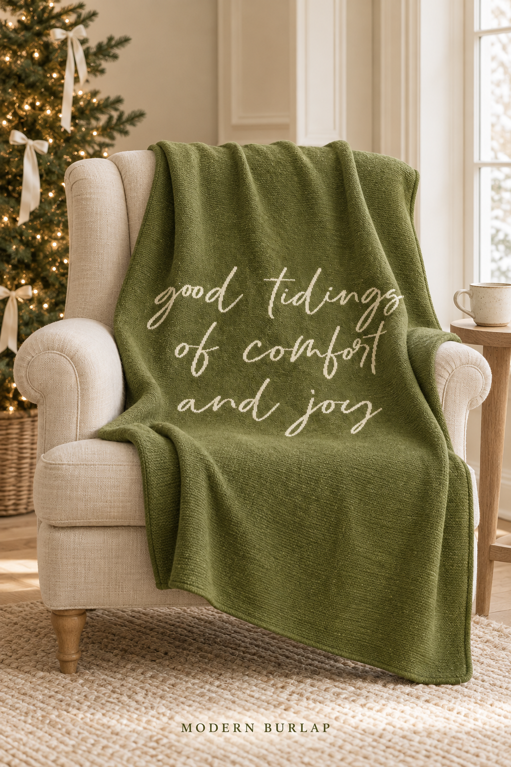 Good Tidings of Comfort and Joy throw in Kaki Green, draped over an ivory armchair beside a Christmas tree. Lifestyle styling.