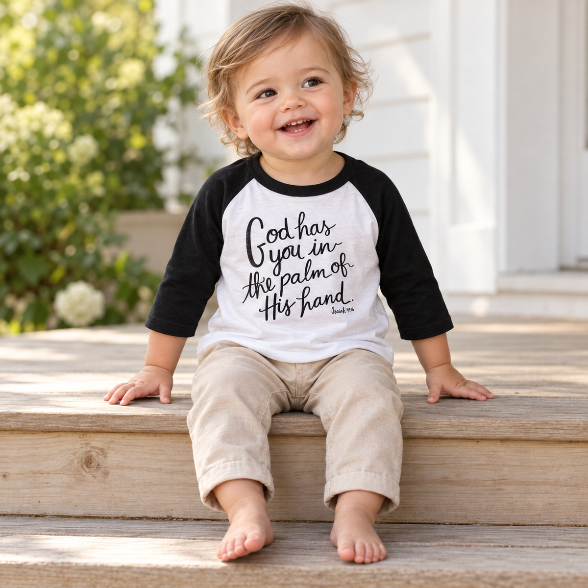 AI-styled toddler wearing the Isaiah 49:16 black and white raglan tee on a porch