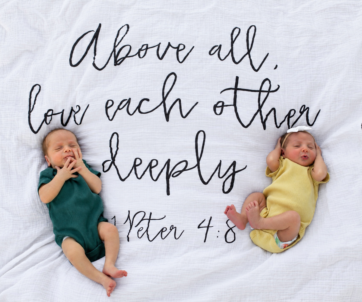 Two babies lying on the 1 Peter 4:8 Scripture swaddle, showing the printed design and fabric.