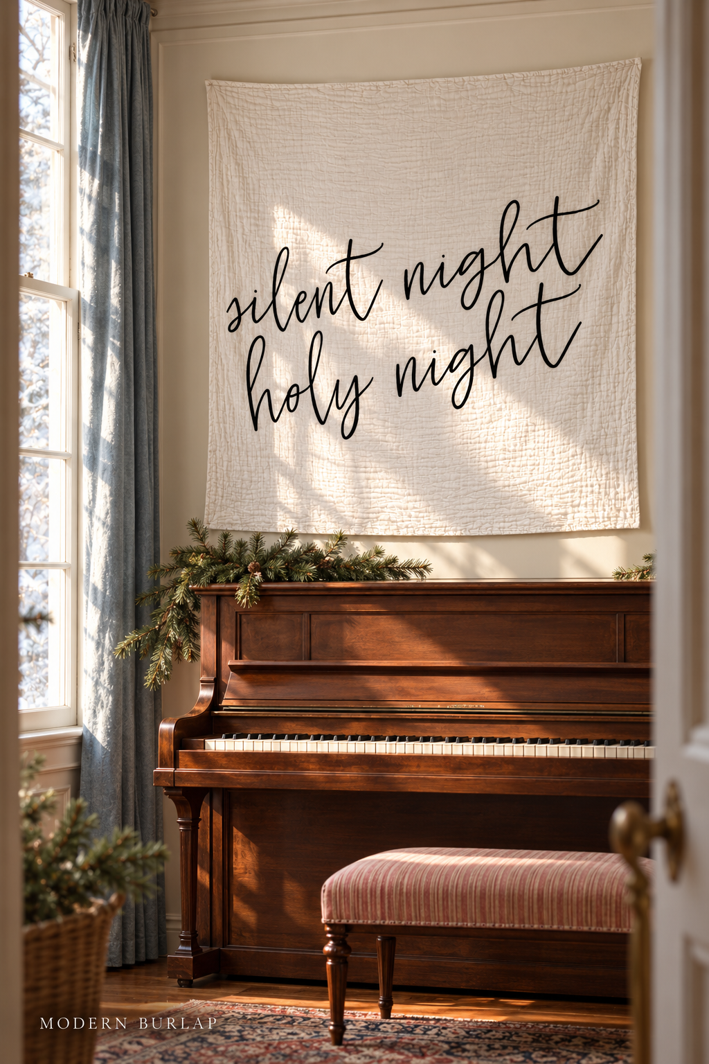 Silent Night Holy Night white muslin swaddle above a walnut piano in a sunlit Christmas room. Modern Burlap wordmark at the bottom.