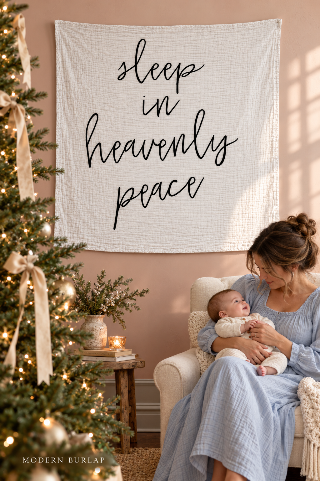 Sleep in Heavenly Peace white muslin swaddle on a blush wall beside a mother holding an awake baby and a Christmas tree. Modern Burlap wordmark at the bottom.