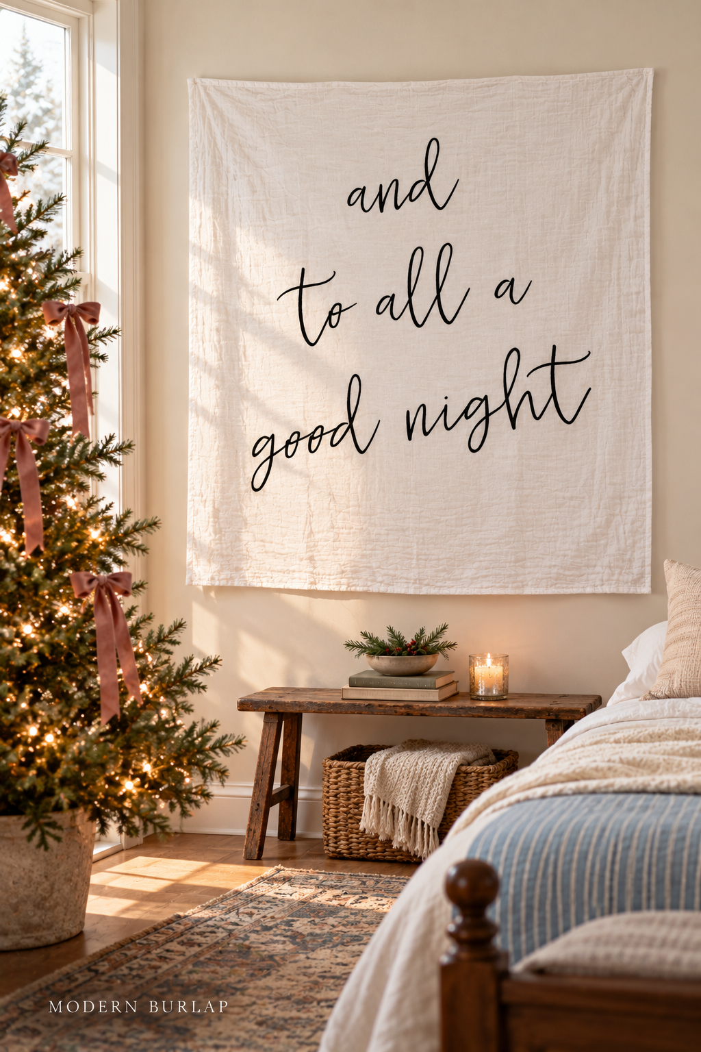 And to All a Good Night white muslin swaddle on a cream wall in a Christmas guest bedroom. Modern Burlap wordmark at the bottom.