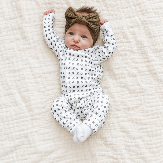 Baby wearing the black-and-white XO organic button coverall on ivory muslin; AI-enhanced lifestyle photograph.