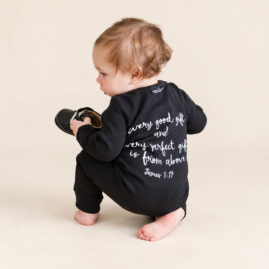 James 1:17 Organic Button Coverall worn by a child against a warm ivory background; AI-enhanced from original product photography.