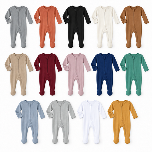 Fourteen solid-color organic zip footies arranged on white, showing the full color range and fold-over hand covers.