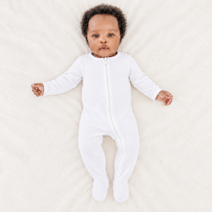 Baby wearing the White organic thermal zip footie, full front view with covered feet; AI-enhanced product image.