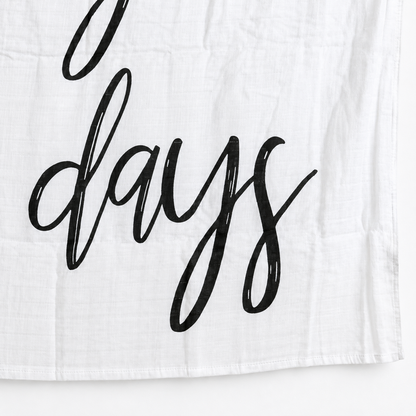 Close view of black calligraphy, white cotton muslin and the hem of These Are the Good Ol' Days swaddle.