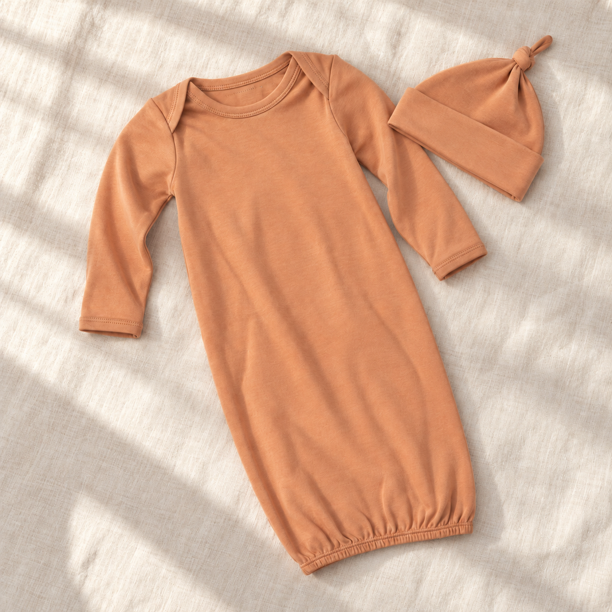 Dusty Coral organic gown and matching knot hat on ivory linen, showing envelope neckline and elastic hem.