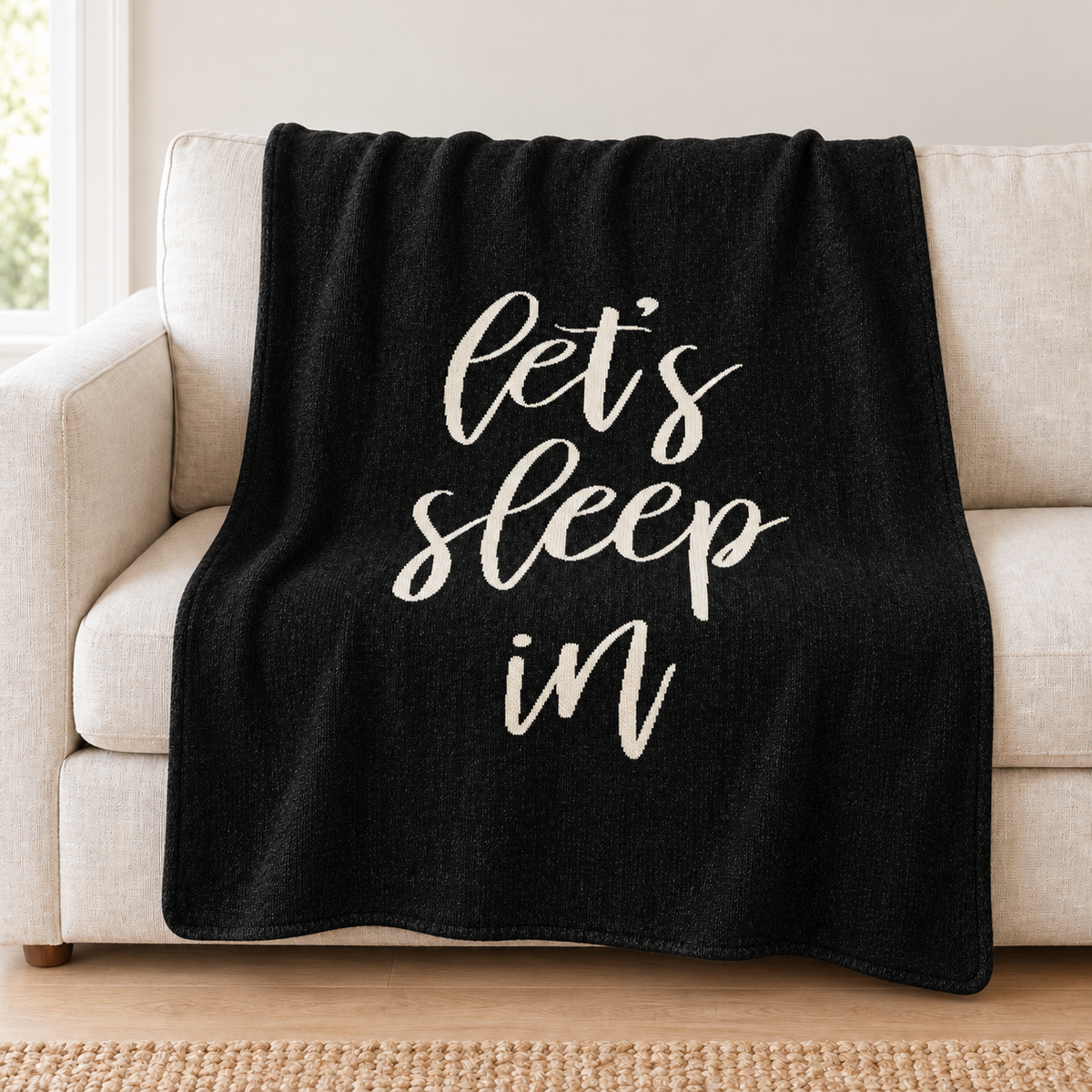 Let's Sleep In knit throw in Black draped over an ivory sofa.