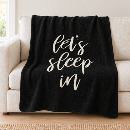 Let's Sleep In knit throw in Black draped over an ivory sofa.