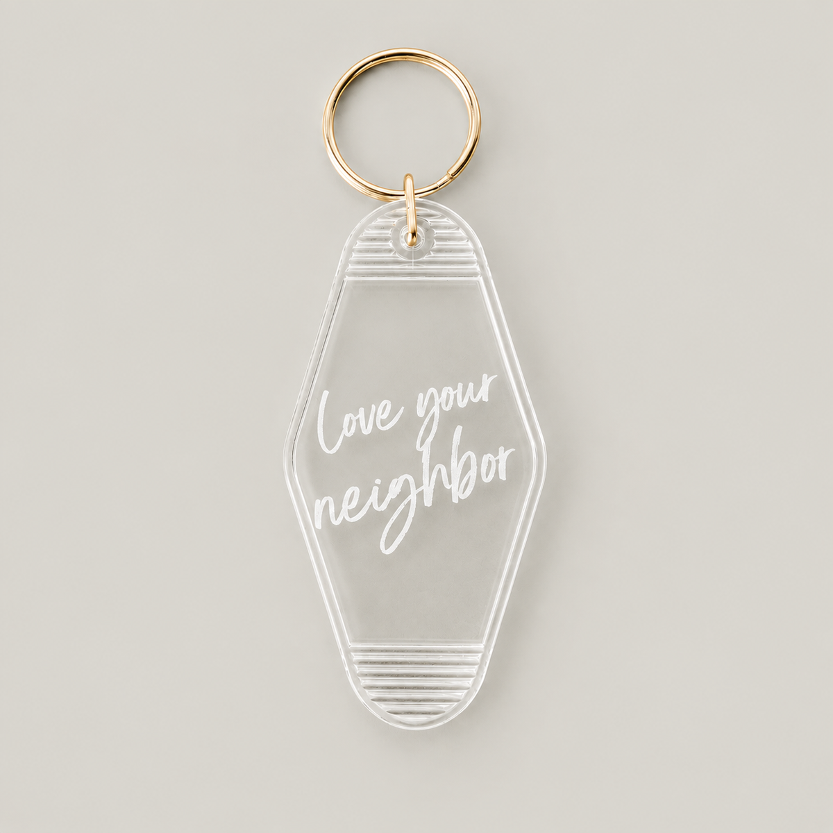 Love your neighbor clear vintage keychain with white script lettering and a gold split ring, front studio view.