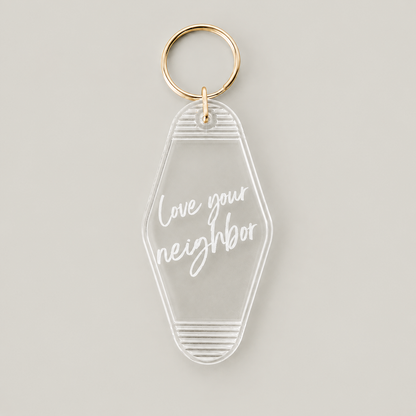 Love your neighbor clear vintage keychain with white script lettering and a gold split ring, front studio view.