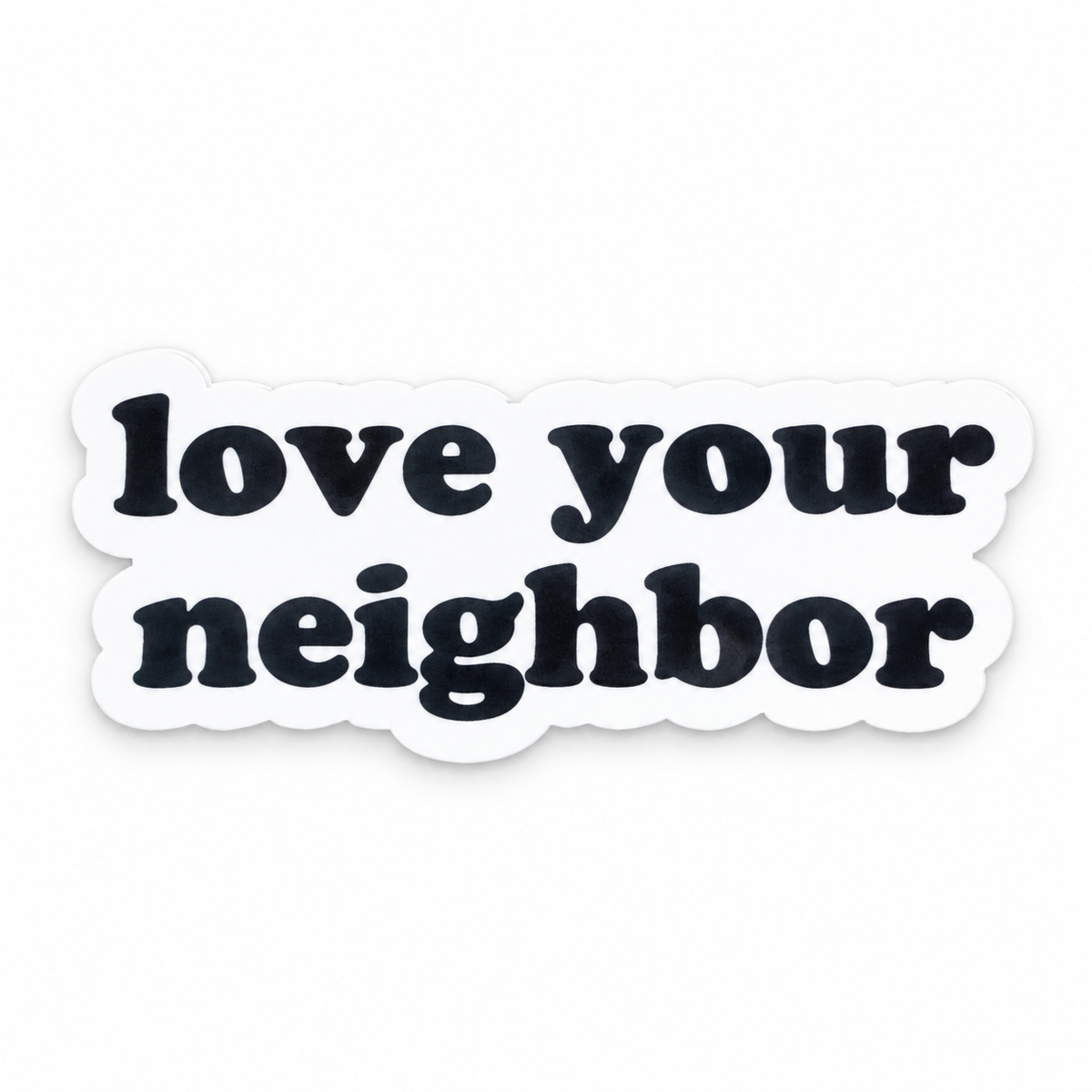 Love your neighbor magnet, black original lettering and white die-cut border, front studio view.