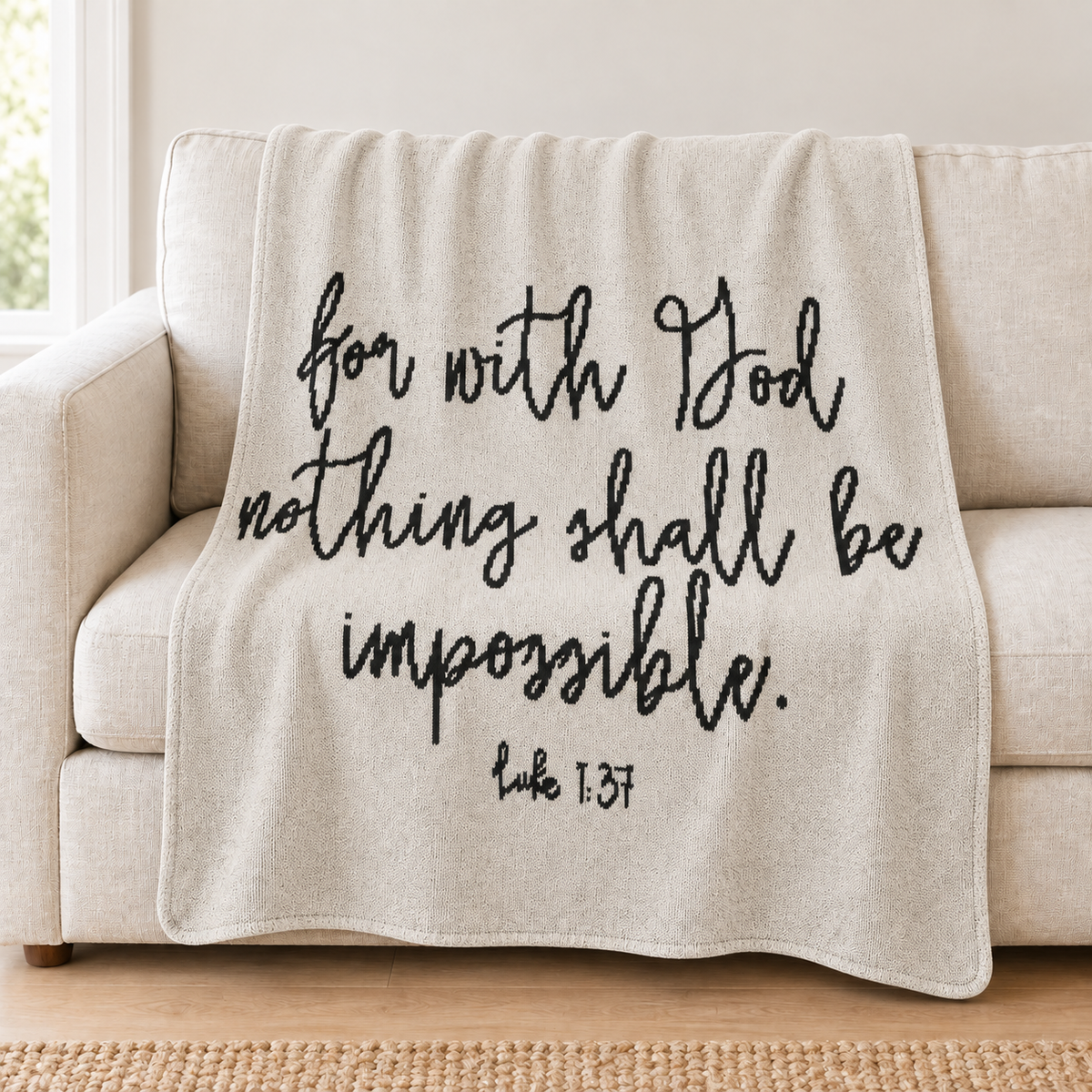 Luke 1:37 natural ivory knit throw with black lettering draped over an ivory sofa.