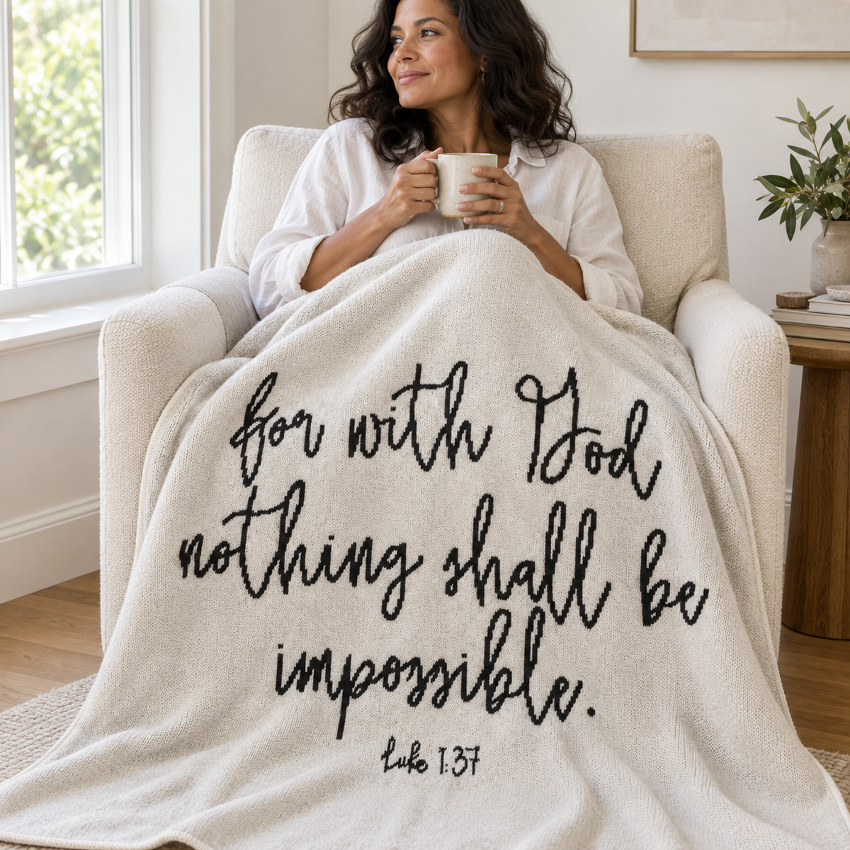 Woman relaxing in an armchair with a Natural Luke 1:37 knit throw.