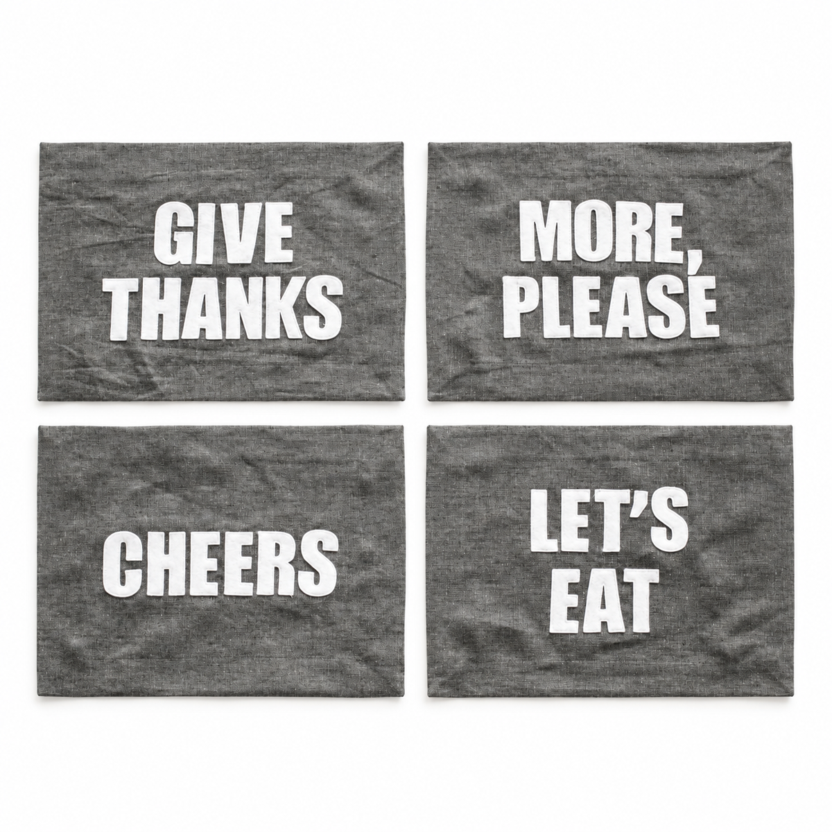 Four graphite linen placemat phrase options: Let's Eat, Cheers, Give Thanks, and More Please. Each sold separately.