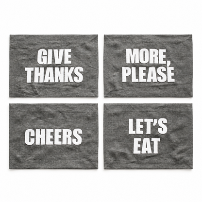 Four graphite linen placemat phrase options: Let's Eat, Cheers, Give Thanks, and More Please. Each sold separately.