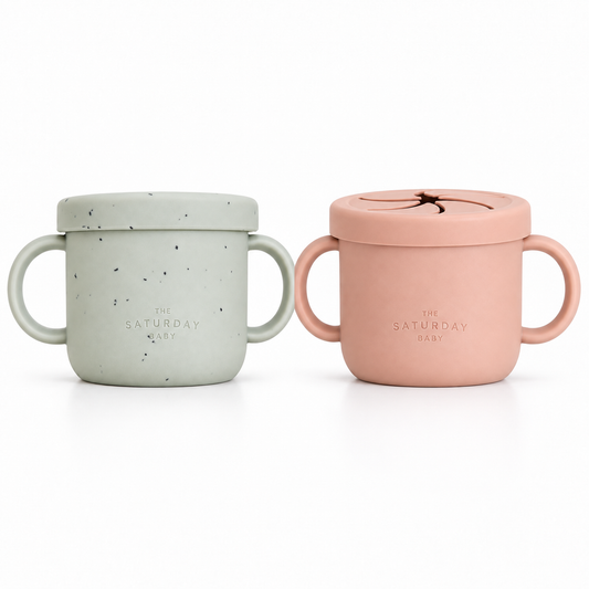 The Saturday Baby silicone snack cups in Sage and Coral at matching scale; sold individually.
