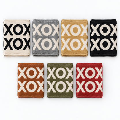 Seven folded XO knit blanket colors: Natural, Aluminum, Straw, Black, Caramel, Kaki Green and Rust Red. Each blanket sold separately.