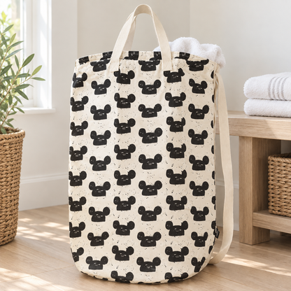 Modern Mouse ivory canvas laundry bag with distressed black print, styled with a white towel beside a wooden bench.