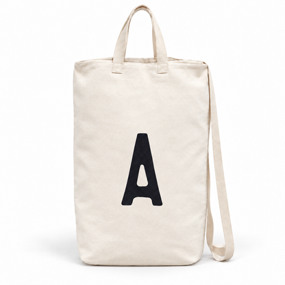 A initial ivory cotton canvas bag with carrying handles and shoulder strap on white