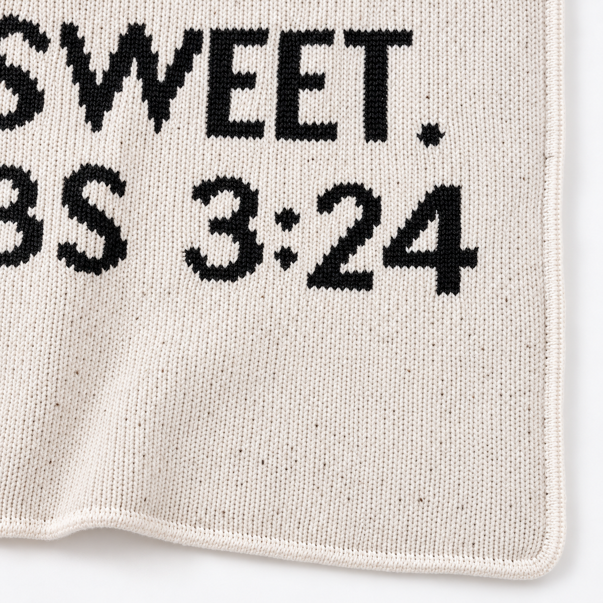 Close view of the Proverbs 3:24 blanket's natural ivory knit, black lettering, and finished corner.