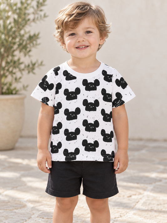 Child wearing a white mouse-head-print tee and black shorts outdoors.