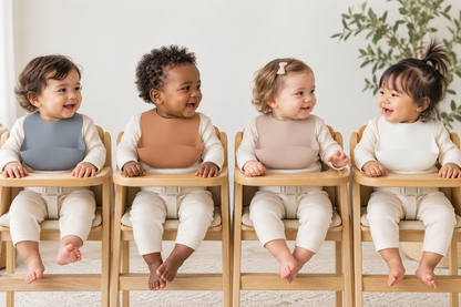 AI-styled lifestyle scene: babies wearing silicone bibs in Sky, Coco, Sand, Cloud, from left to right. Colors sold separately.