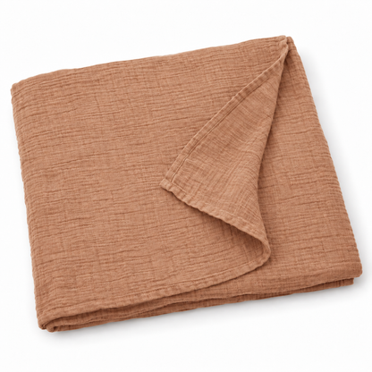Ginger organic cotton muslin swaddle folded on white, with a turned corner showing the fine weave and hem.