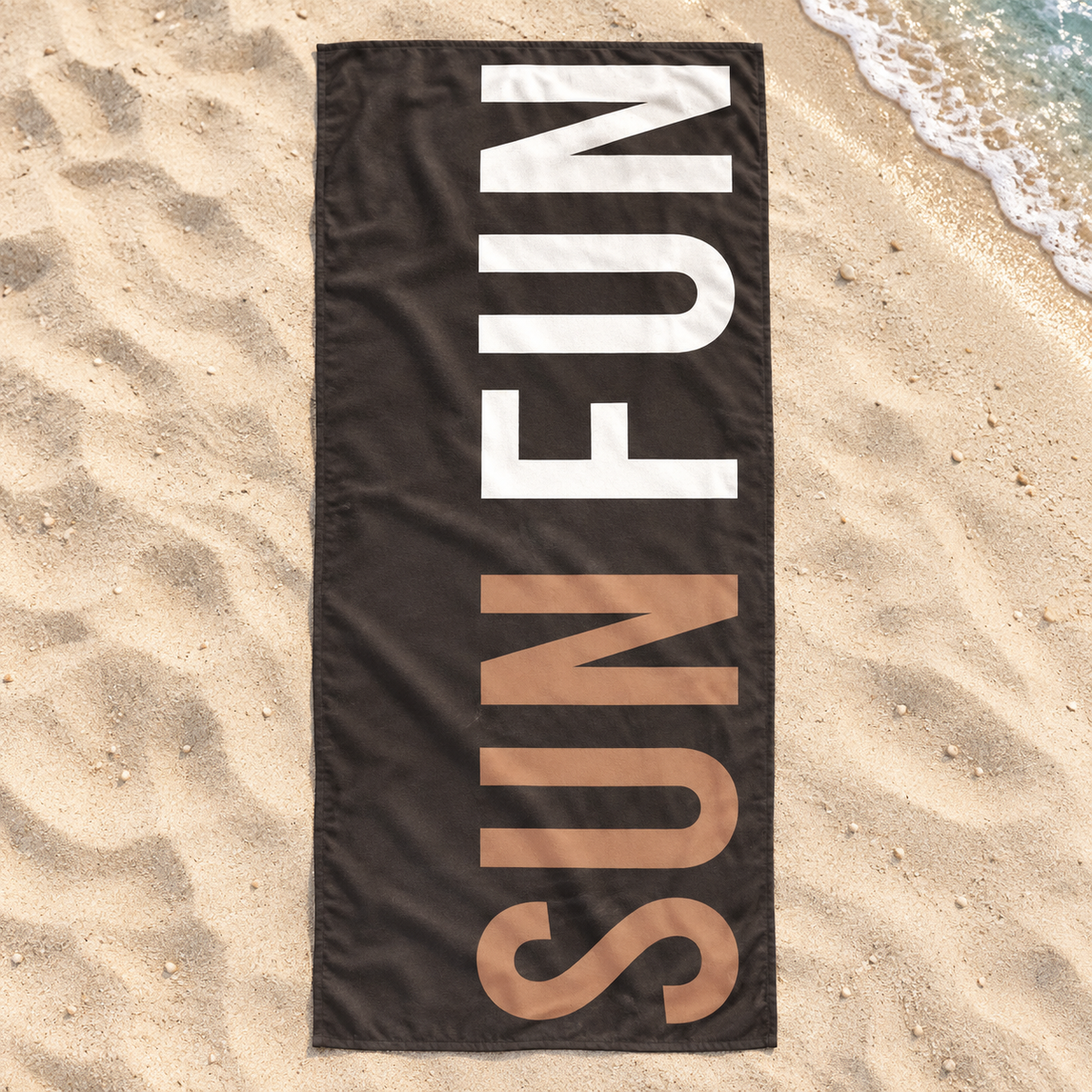 Dark Sun Fun quick-dry towel with tan and white lettering, shown open on beach sand.