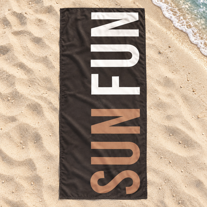 Dark Sun Fun quick-dry towel with tan and white lettering, shown open on beach sand.