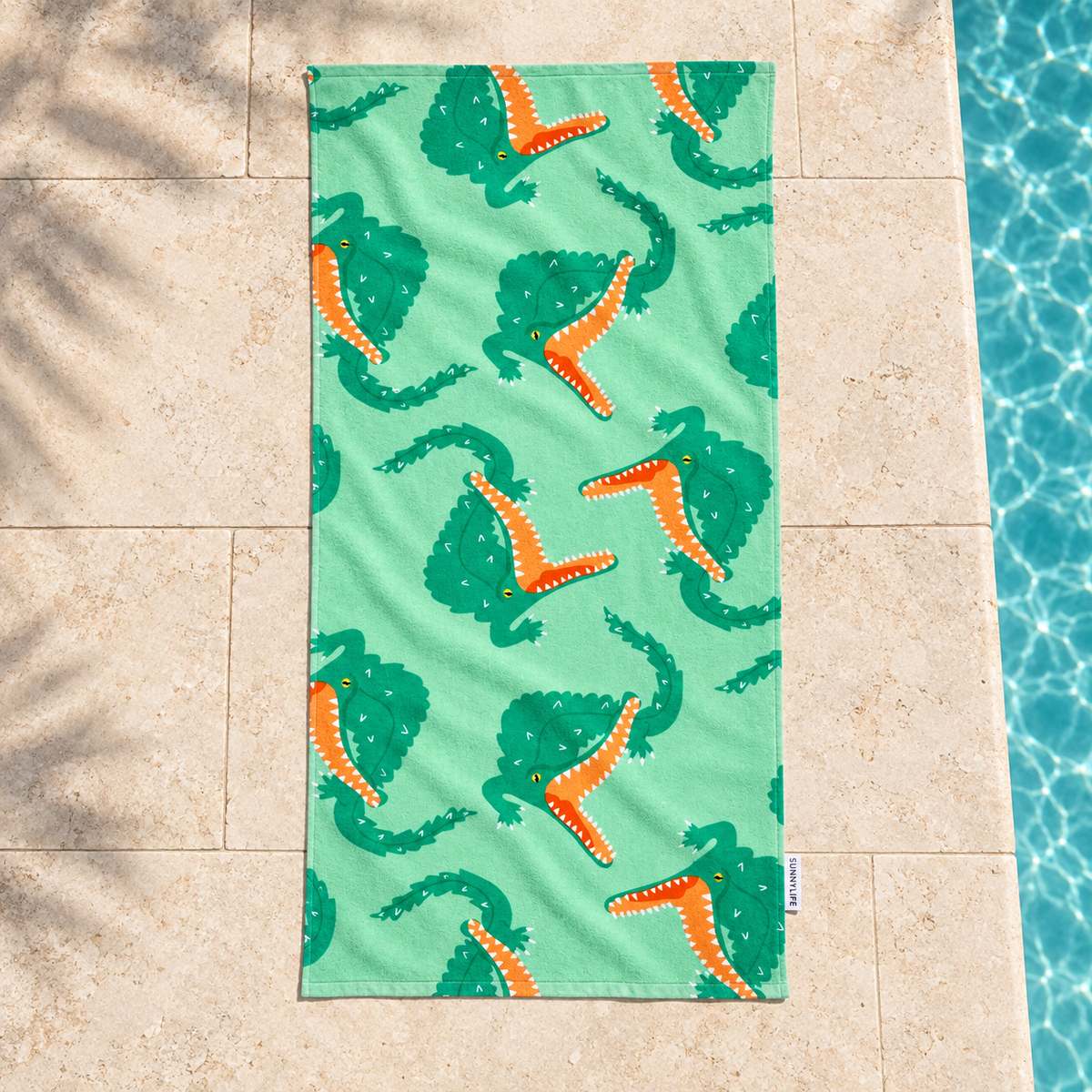 Sunnylife Croc kids towel with green crocodiles and orange mouths, shown beside a pool.