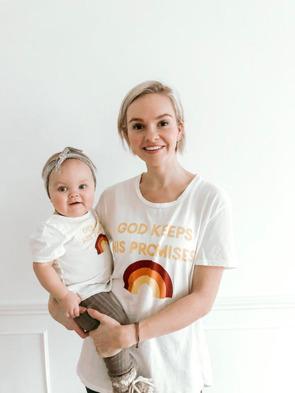 Mother holding a child while both wear white God Keeps His Promises rainbow tees.