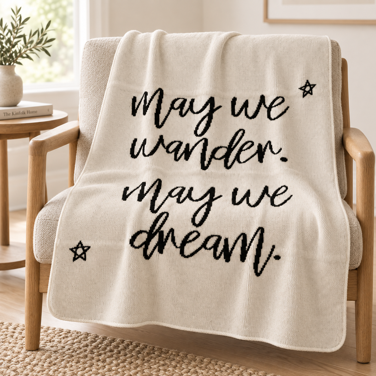 Natural May We Wander May We Dream recycled cotton blanket styled over a small oak reading chair, showing the black script and stars.