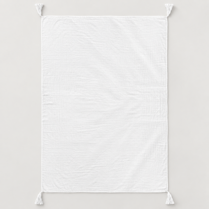 White organic cotton muslin throw shown fully open with four corner tassels on a pale gray background.