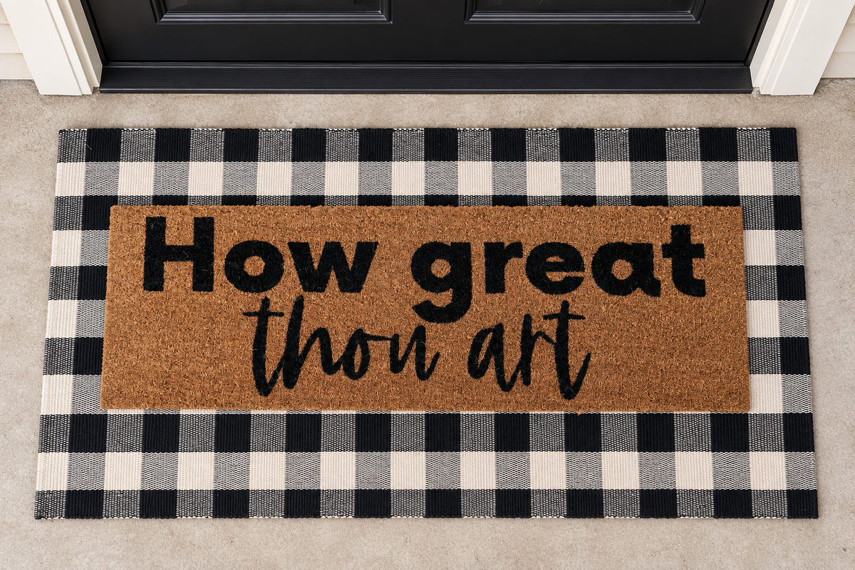 XL Christian Doormat | How Great Thou Art layered over a black and ivory buffalo plaid runner at a black door.