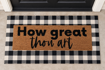 XL Christian Doormat | How Great Thou Art layered over a black and ivory buffalo plaid runner at a black door.